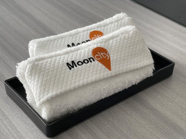 Two white towels with "Mooncity" embroidered on them, placed on a black tray. - Mooncity Hotel & Boardinghouse (Frankfurt)