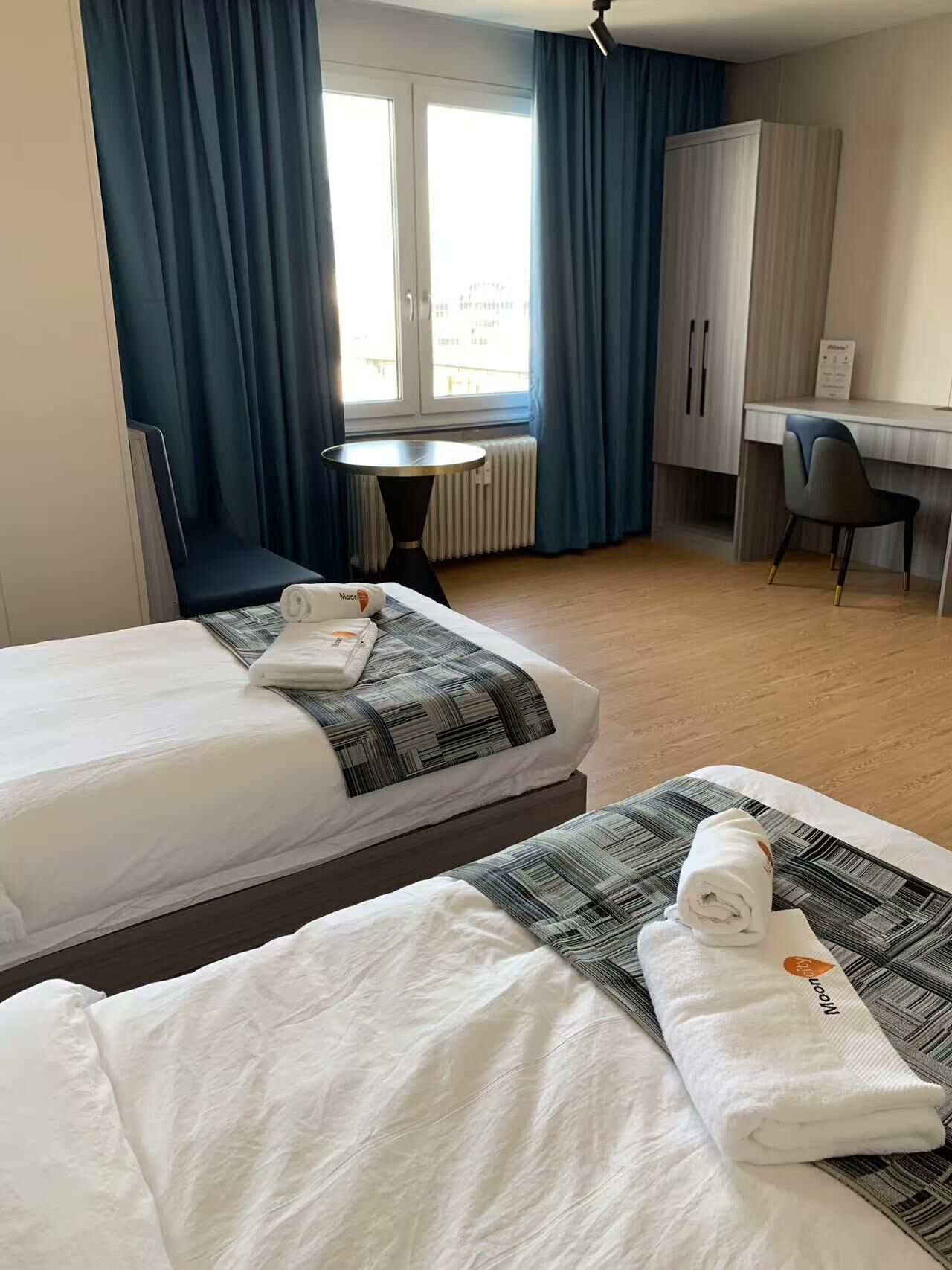 Habitación de hotel con dos camas, un escritorio, una silla y vistas de la ciudad desde la ventana.