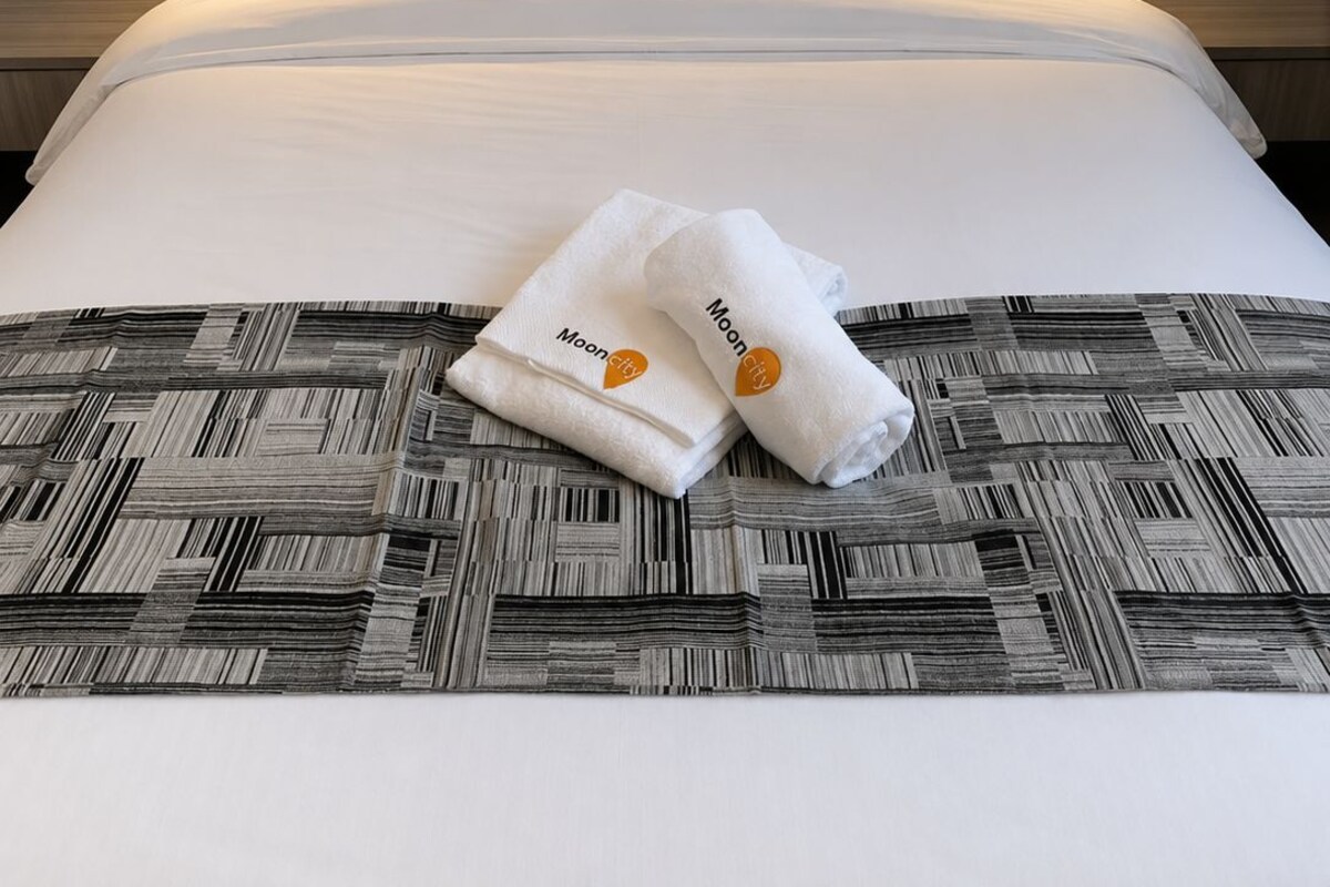 A hotel room with a large bed, two pillows, a headboard, and a wall-mounted light fixture.