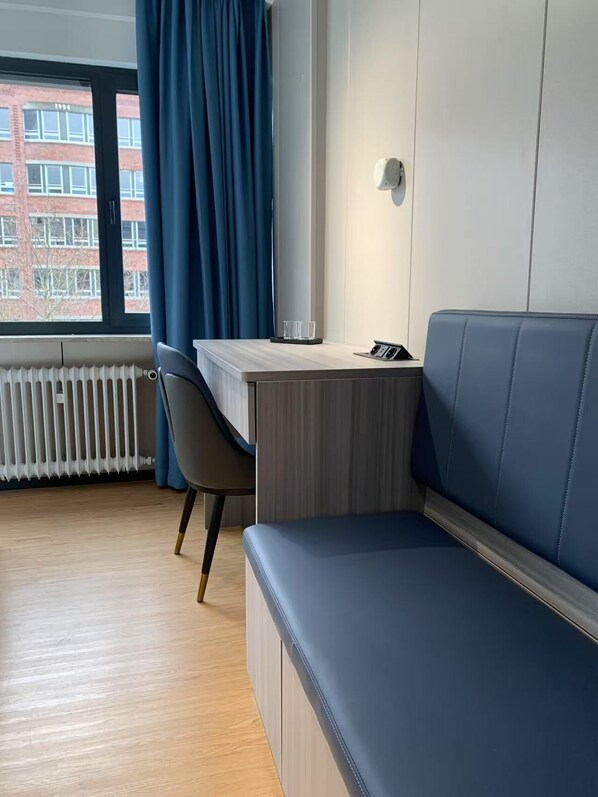 A modern room with a wooden desk, a blue sofa, a chair, and a radiator. - Mooncity Hotel & Boardinghouse (Frankfurt)