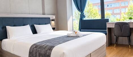 A modern hotel room with a large bed, a desk, and a view of buildings outside.