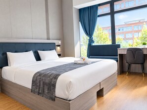 A modern hotel room with a large bed, a desk, and a view of buildings outside. - Mooncity Hotel & Boardinghouse (Frankfurt)