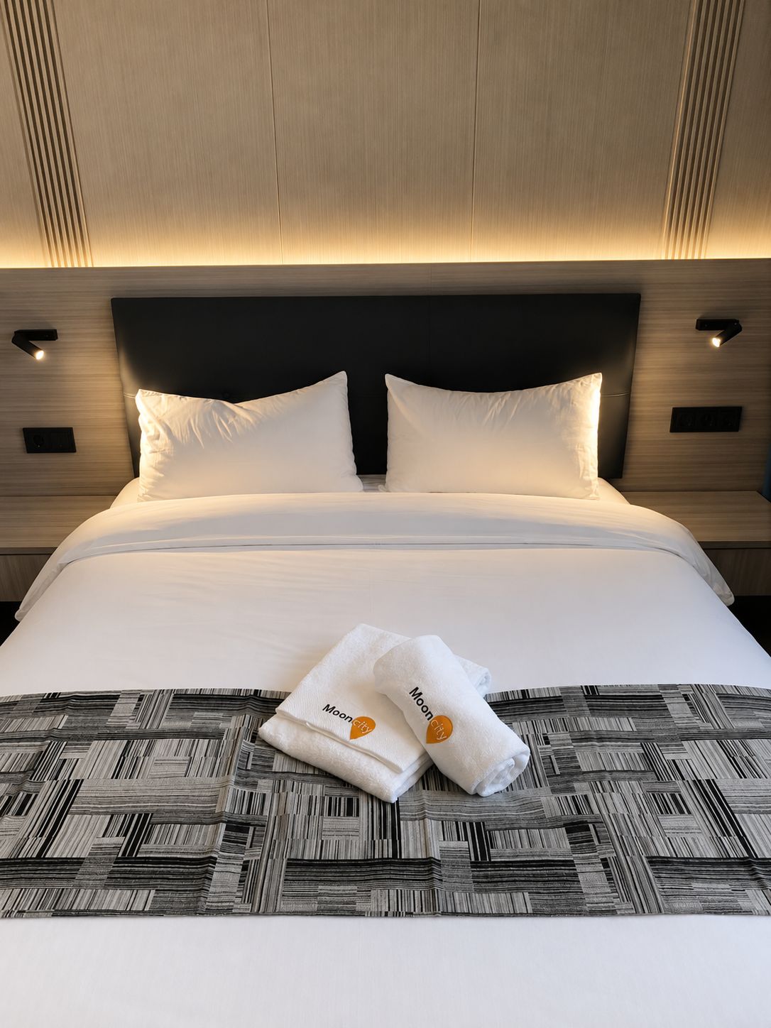 Une chambre d’hôtel avec un grand lit, deux oreillers, une tête de lit et un luminaire fixé au mur.