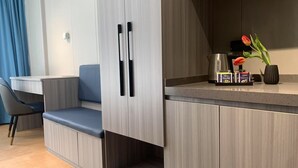 Una habitación de hotel moderna con kitchenette, una zona de estar con un banco acolchado azul y una pequeña mesa.