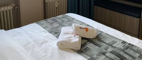 Una habitación de hotel con una cama, un ventanal con cortinas, un radiador y un banco.