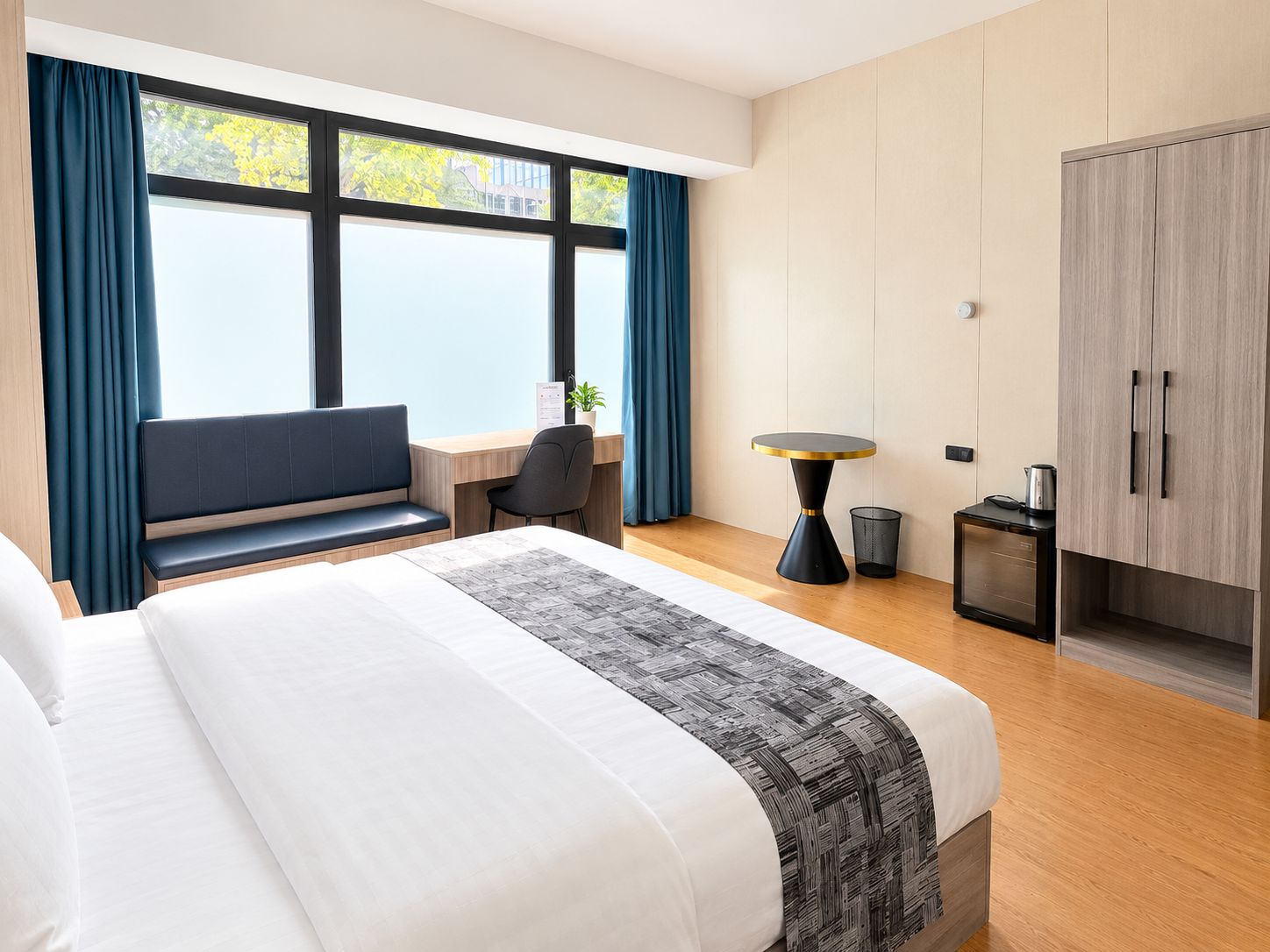 Habitación de hotel con una cama grande, un escritorio, una silla, una mesita y un armario.