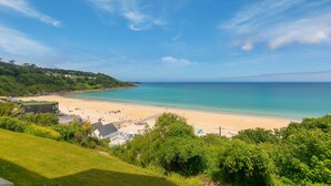A coastal beach with a clear sky, sandy shore, and lush greenery in the foreground.