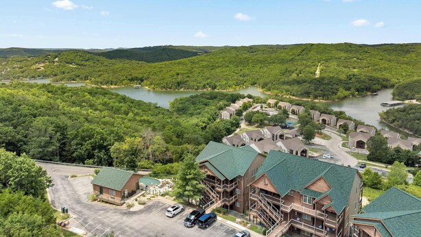 A lodge with multiple buildings, a parking area, and a view of a lake surrounded by forested hills.