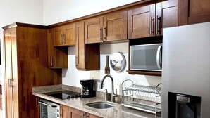 A kitchen with wooden cabinets, a stainless steel refrigerator, a built-in oven, a microwave, a sink, and a dish drying rack. - Coastal Comfort: Spacious Second-Floor Getaway (Playas Del Coco)