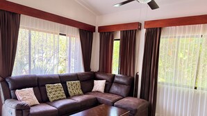 A living room with a sectional sofa, a wooden coffee table, and large windows with curtains. - Coastal Comfort: Spacious Second-Floor Getaway (Playas Del Coco)