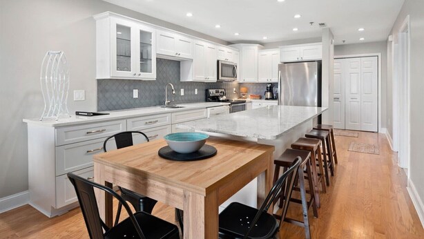 Une cuisine moderne avec des meubles blancs, un îlot central et un coin repas doté de chaises en bois.