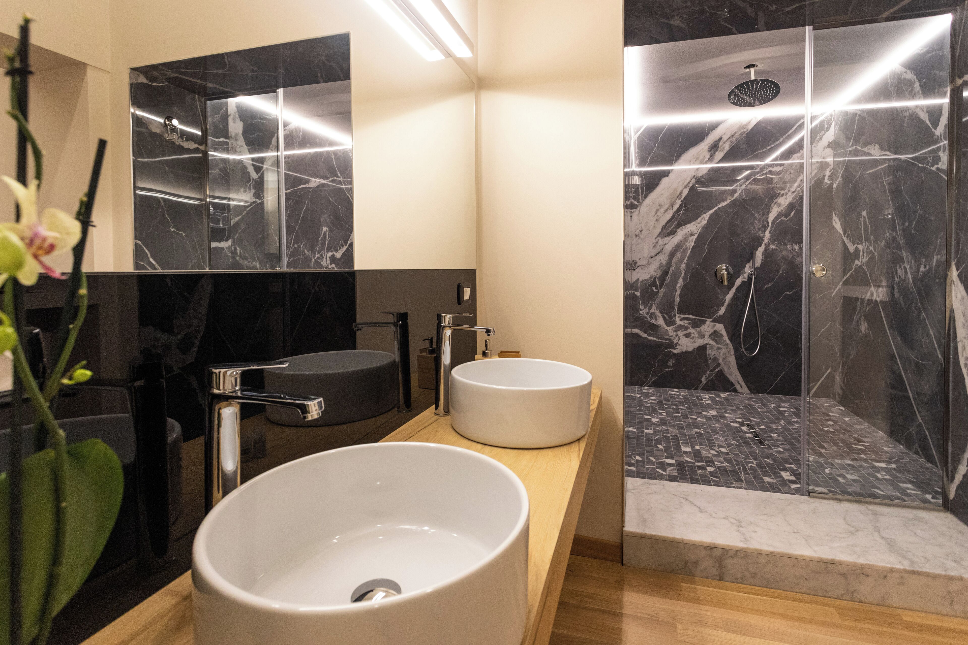 Un baño moderno con dos lavamanos, ducha y paredes de mármol.