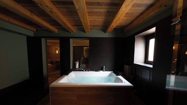 A modern bathroom with a freestanding bathtub, wooden beams on the ceiling, and dark walls. - Divisi Suites & SPA (Palermo)