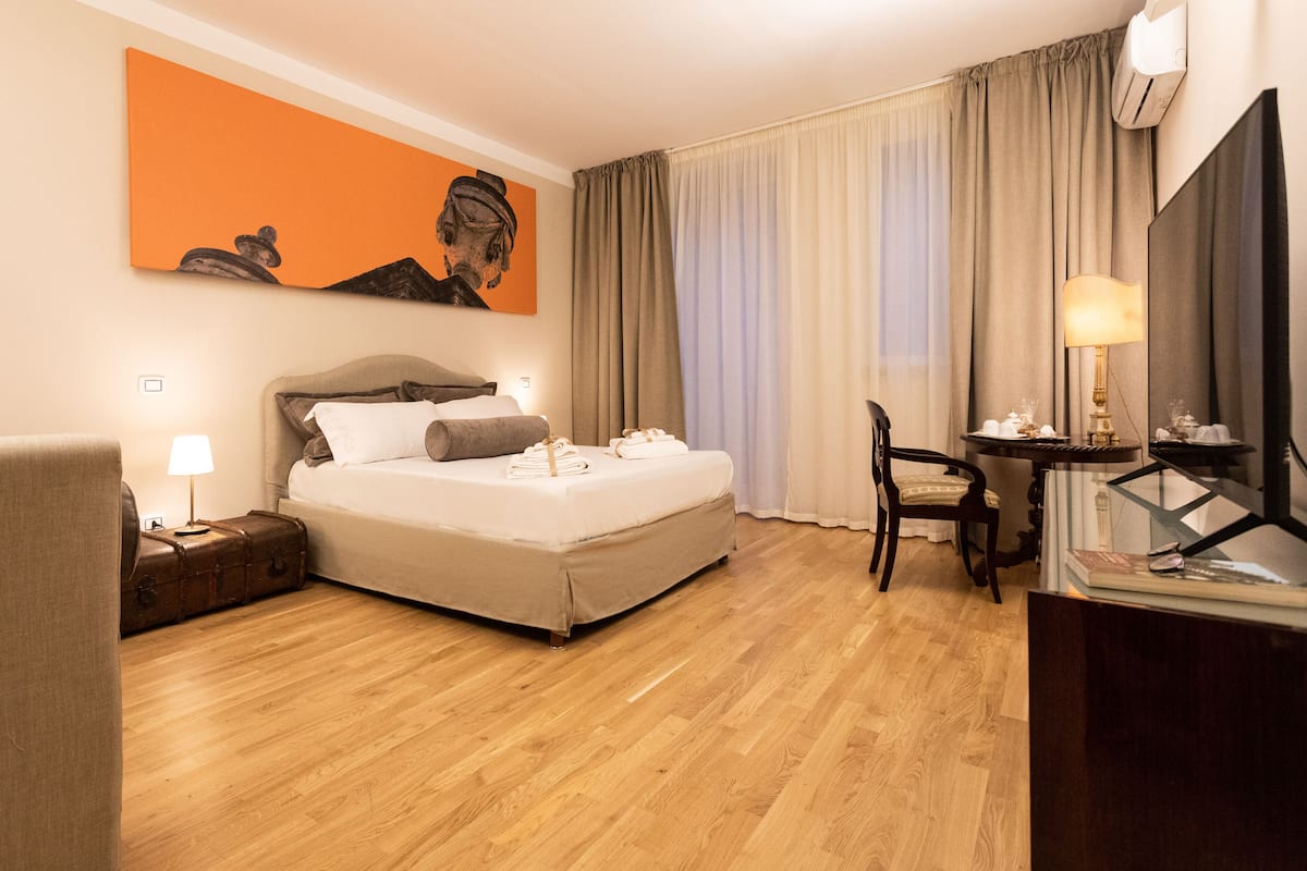 A hotel room with a bed, a desk, a chair, a lamp, and a painting on the wall.
