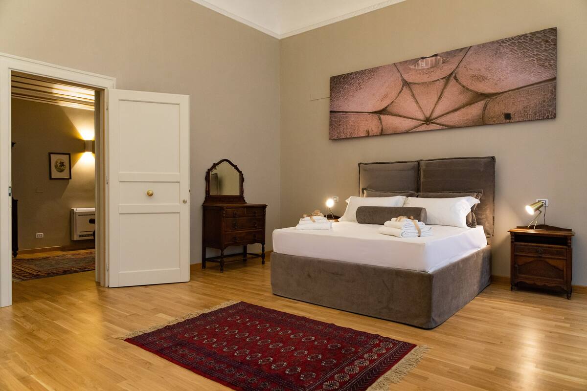 A bedroom with a large bed, a dresser, a mirror, and a painting on the wall.