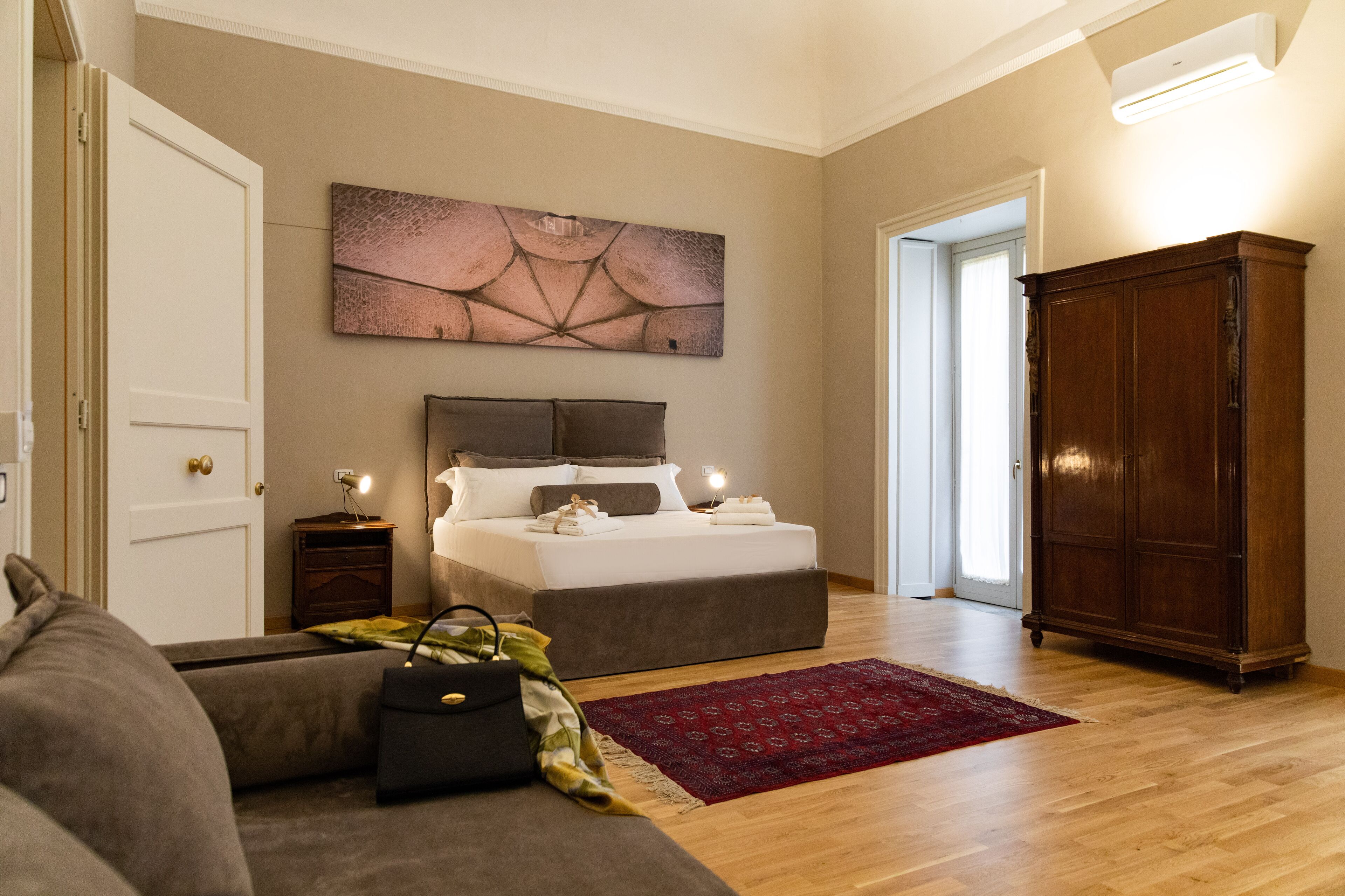 Un dormitorio con cama, armario de madera, alfombra roja y un cuadro en la pared.