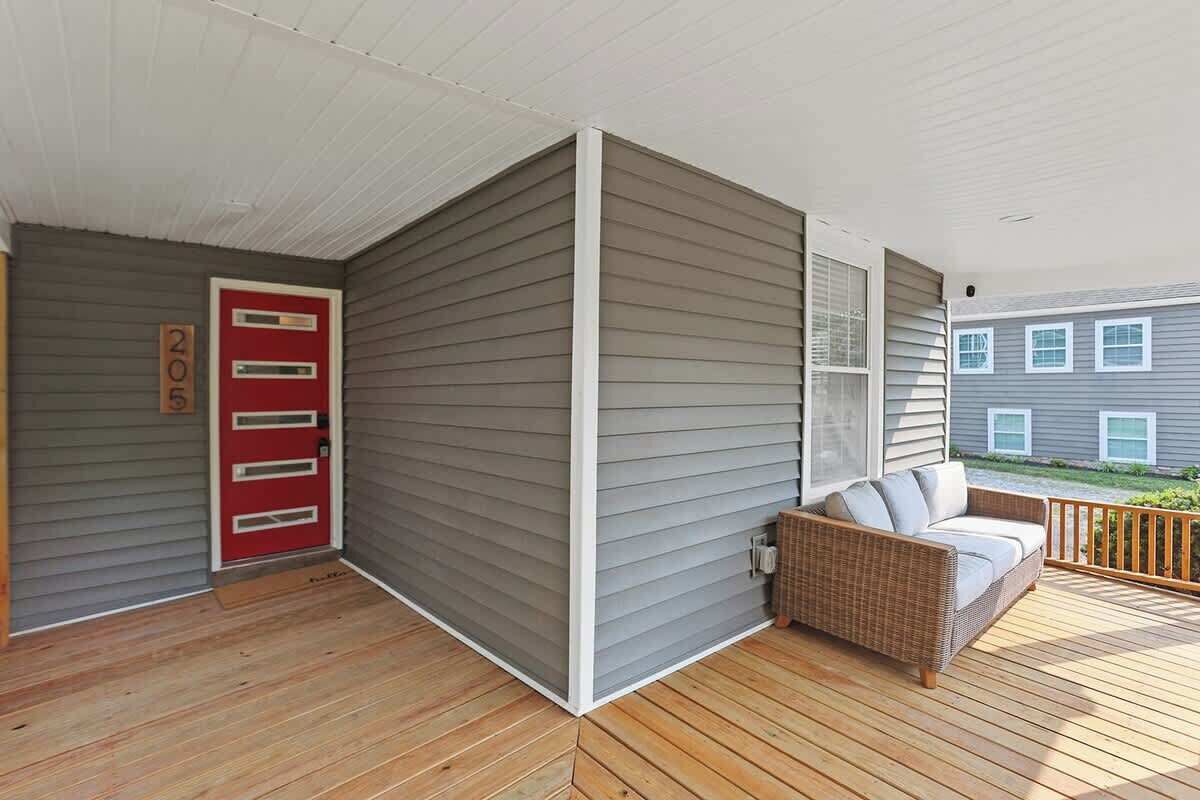 A covered porch with a red door, a wicker sofa, and a wooden deck.
