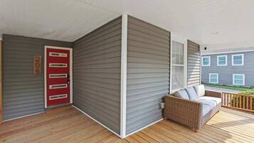 A covered porch with a red door, a wicker sofa, and a wooden deck.
