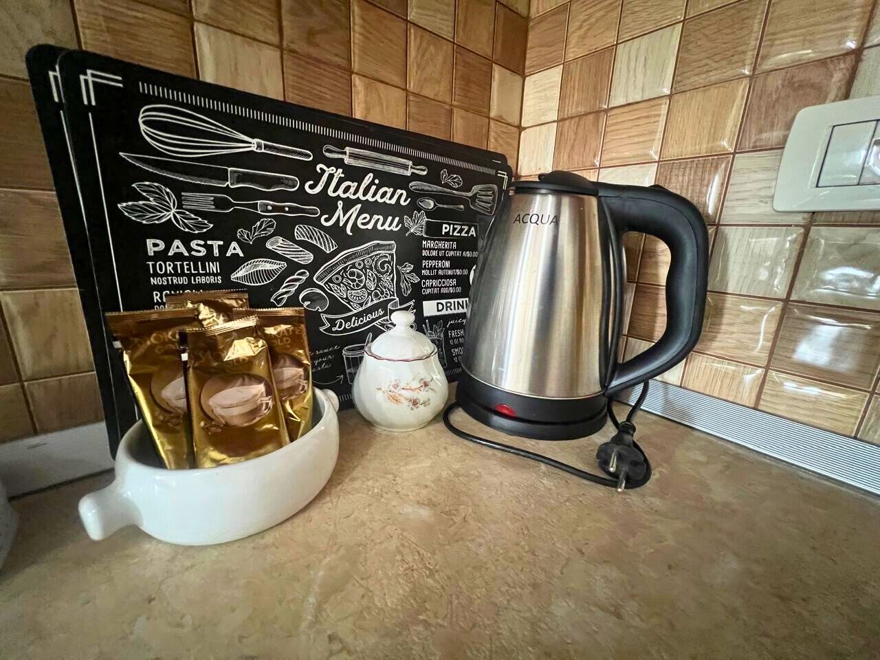 A kitchen counter with a blackboard menu, a white teapot, a coffee pot, and packets of pasta.