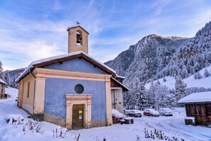 Une petite église dotée d’un clocher, entourée d’arbres et de montagnes couverts de neige.