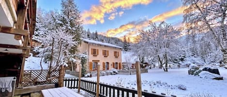 A snow-covered outdoor area with a wooden building, a wooden fence, and a bench.