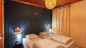 Een kamer met twee bedden, een wandlamp, een klein tafeltje en een plafondlamp.