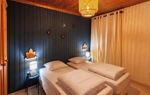 Ein Zimmer mit zwei Betten, einer Wandlampe, einem kleinen Tisch und einer Pendelleuchte.