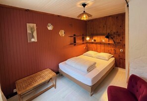 Een slaapkamer met een houten bed, een bankje en een rode stoel.