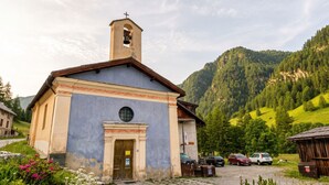 Una pequeña iglesia con un campanario, rodeada de un estacionamiento y un paisaje montañoso.