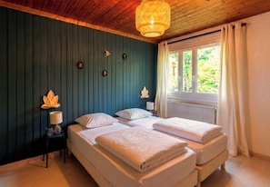 Une chambre avec deux lits, un plafond en bois, une fenêtre avec des rideaux et une lampe fixée au mur.