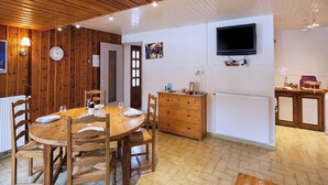 Een kamer met houten lambrisering, een eettafel gedekt voor vier personen, een houten kast, een aan de muur bevestigde televisie en een klok.