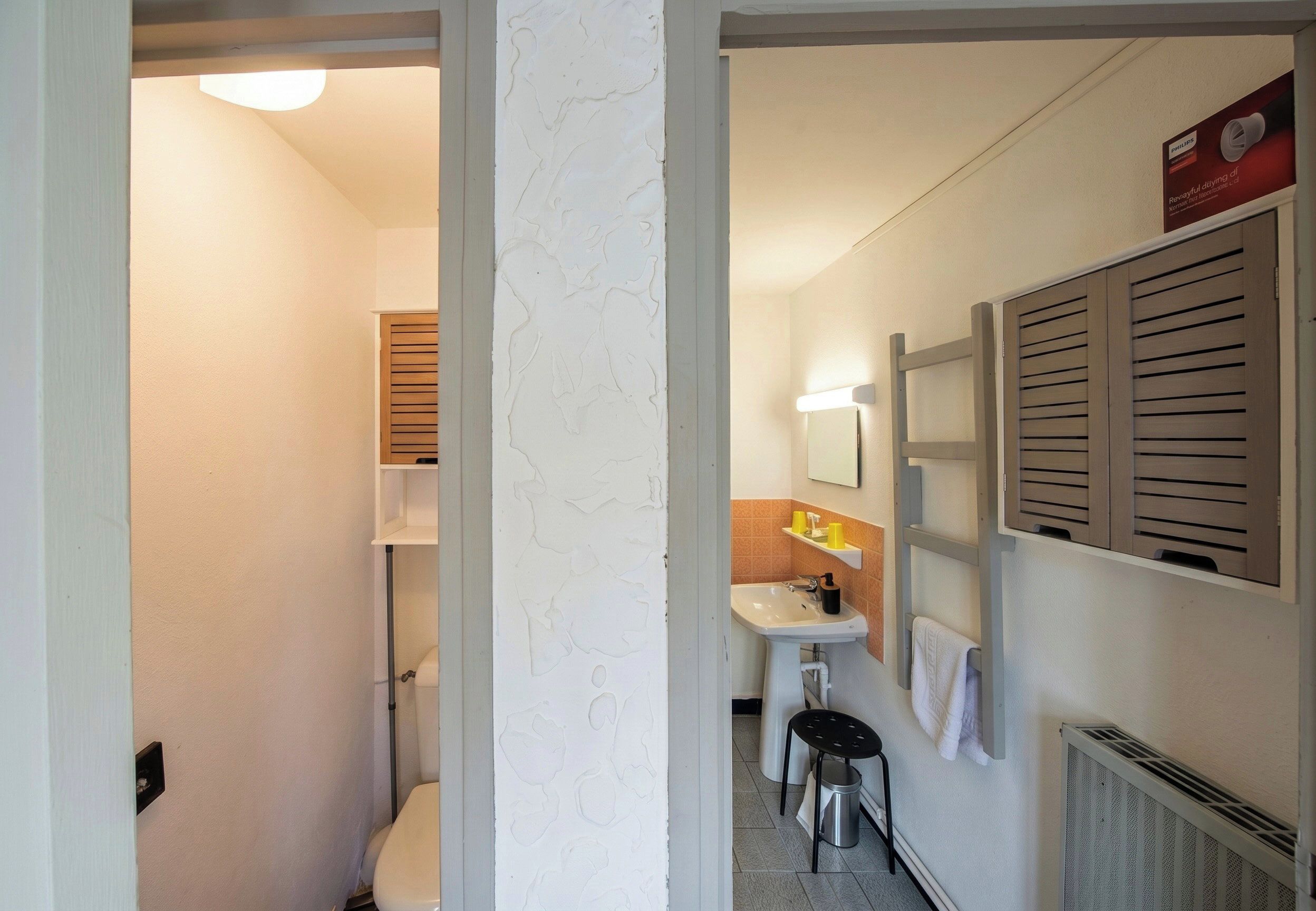 A narrow hallway leading to a bathroom with a toilet, sink, and towel rack.