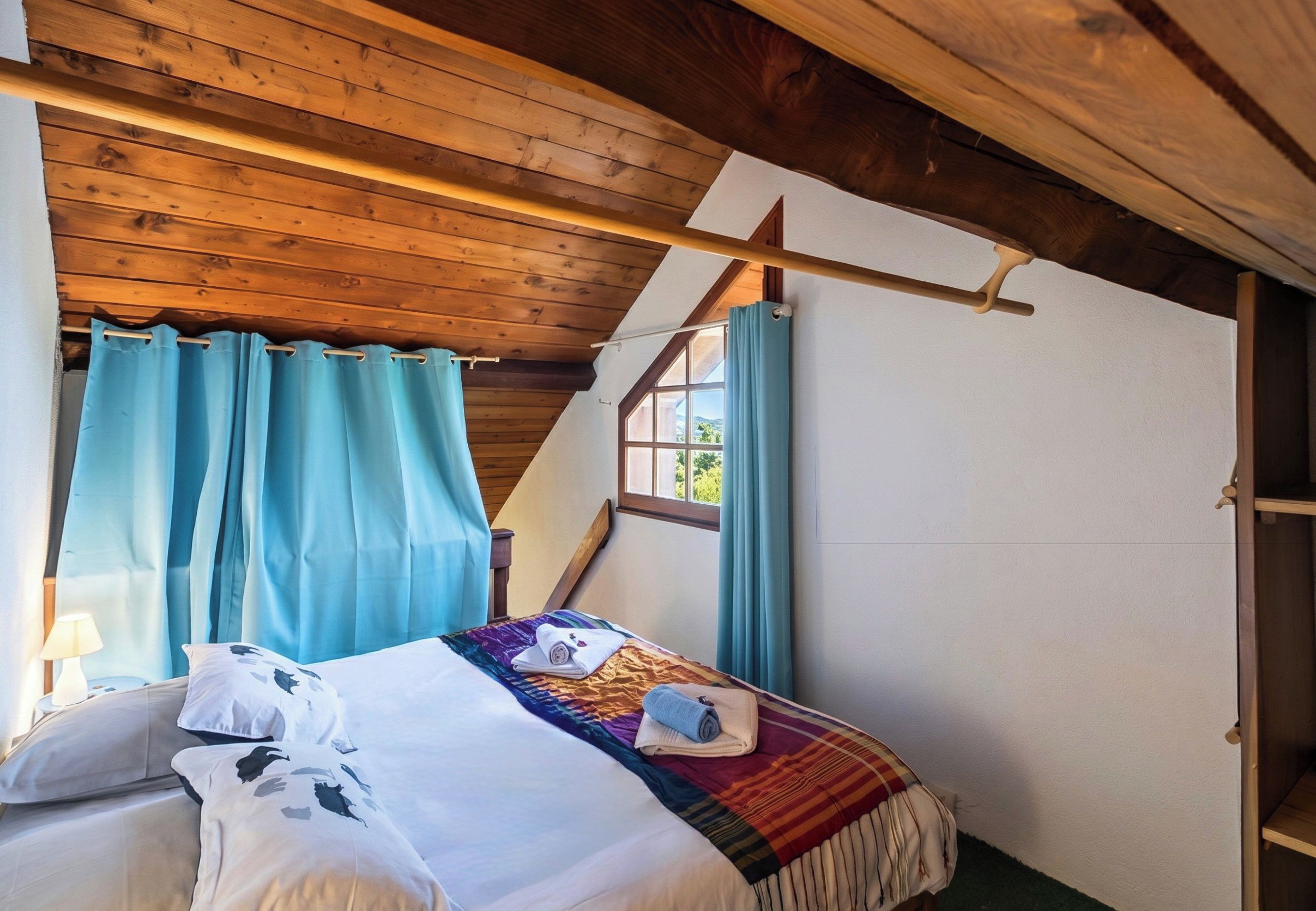 A bedroom with a sloped ceiling, a bed with a colorful blanket, and a window with curtains.