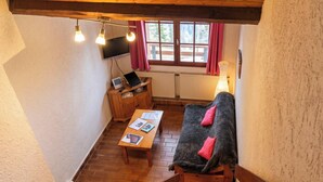 Una habitación acogedora con un banco de madera, una mesa con papeles, un televisor y una ventana con cortinas.
