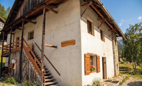 Un bâtiment rustique avec un escalier en bois, une enseigne sur laquelle on peut lire « PERSÉVÉRANCE », et un mur de pierre.