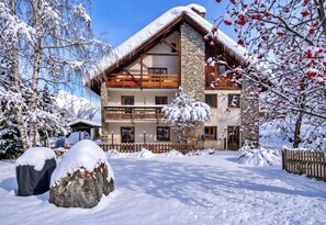 Un chalet à plusieurs étages, doté d’une façade en pierre, de balcons en bois et d’un toit recouvert de neige.