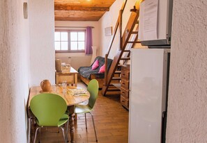 Une pièce chaleureuse avec une table en bois, des chaises, un radiateur, une fenêtre avec des rideaux et une échelle.