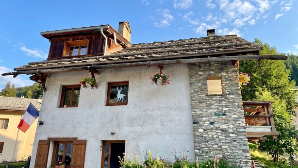 Un edificio de estilo chalete tradicional con fachada de piedra, contraventanas de madera y un balcón.