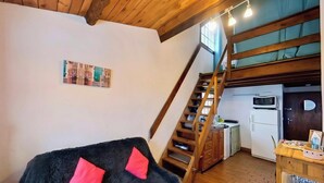Un espacio tipo loft con escalera de madera, una zona de cocina y un rincón de descanso acogedor con un sofá cubierto de piel.