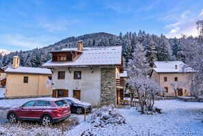 Un edificio su due piani con facciata in pietra e tetto in metallo, circondato da alberi innevati e una montagna sullo sfondo.