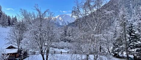 A snow-covered landscape with a cabin, trees, and mountains in the background.