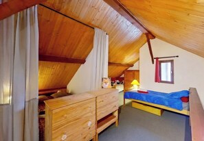 Un pequeño dormitorio en el ático con una cama nido de madera, un aparador de madera y una ventana con cortinas.