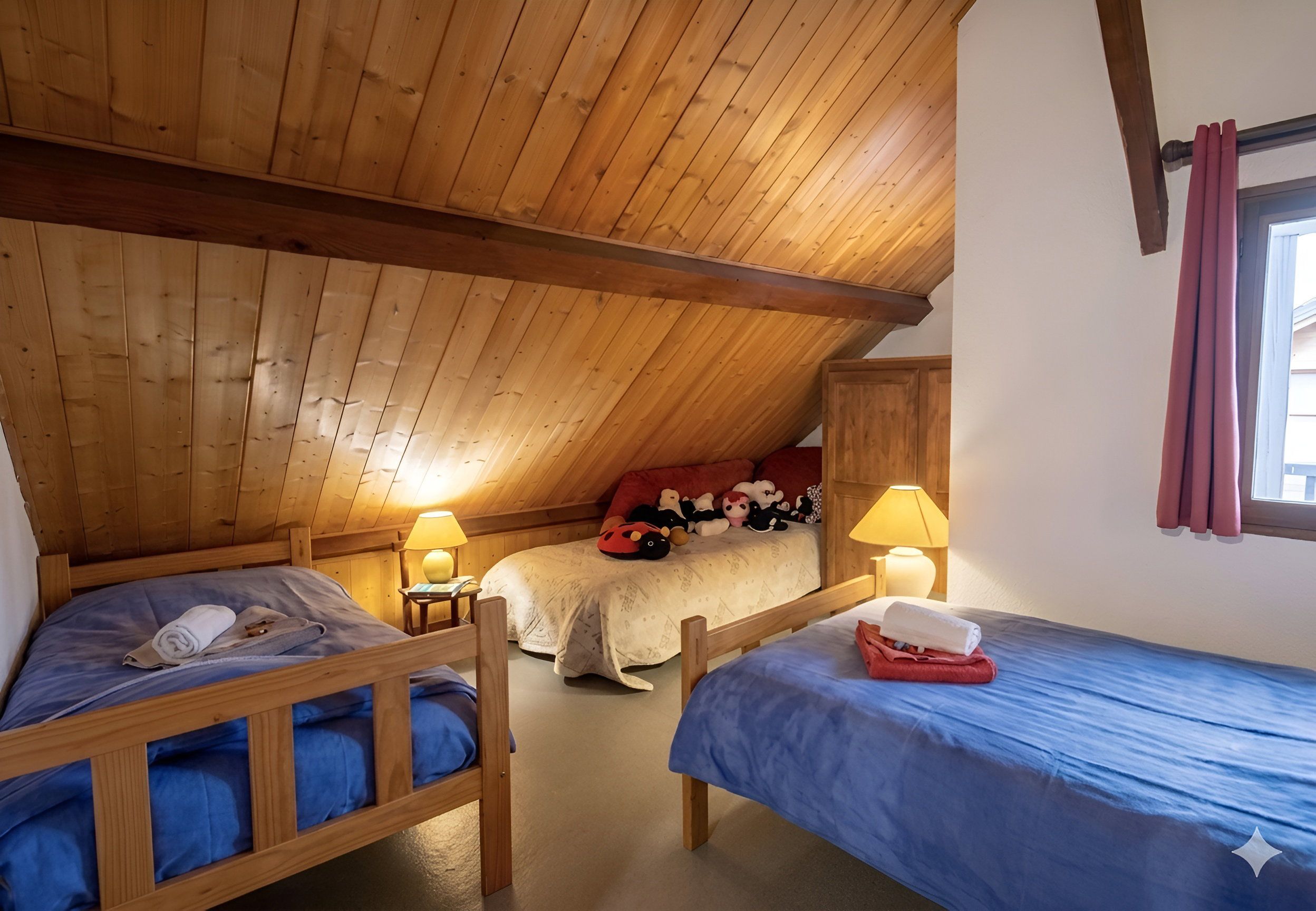 Une chambre mansardée chaleureuse avec trois lits en bois, un plafond en pente et une fenêtre avec des rideaux.