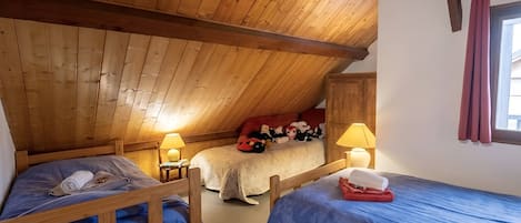 Une chambre mansardée chaleureuse avec trois lits en bois, un plafond en pente et une fenêtre avec des rideaux.