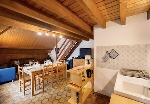 Una habitación acogedora con una mesa de comedor de madera dispuesta para cuatro, una zona de cocina con cafetera y una escalera que sube a un nivel superior.