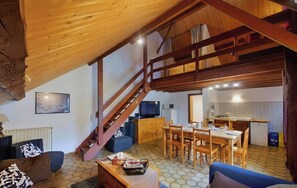 Un salon chaleureux avec un escalier en bois, une table à manger et une cuisine en arrière-plan.