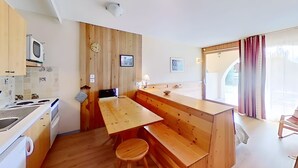 A compact kitchen with wooden accents, a built-in stove, and a small dining area with a bench and stool. - CASA-Joubarbe Super 4p terrasse plein sud Arvieux! (Arvieux)