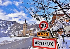 Un panneau de signalisation routière indiquant « 30 » et « D902 », ce qui correspond à une limitation de vitesse et à un numéro de route, avec le nom « ARVIEUX » en dessous, le tout sur un fond représentant un paysage enneigé avec une église et des montagnes.