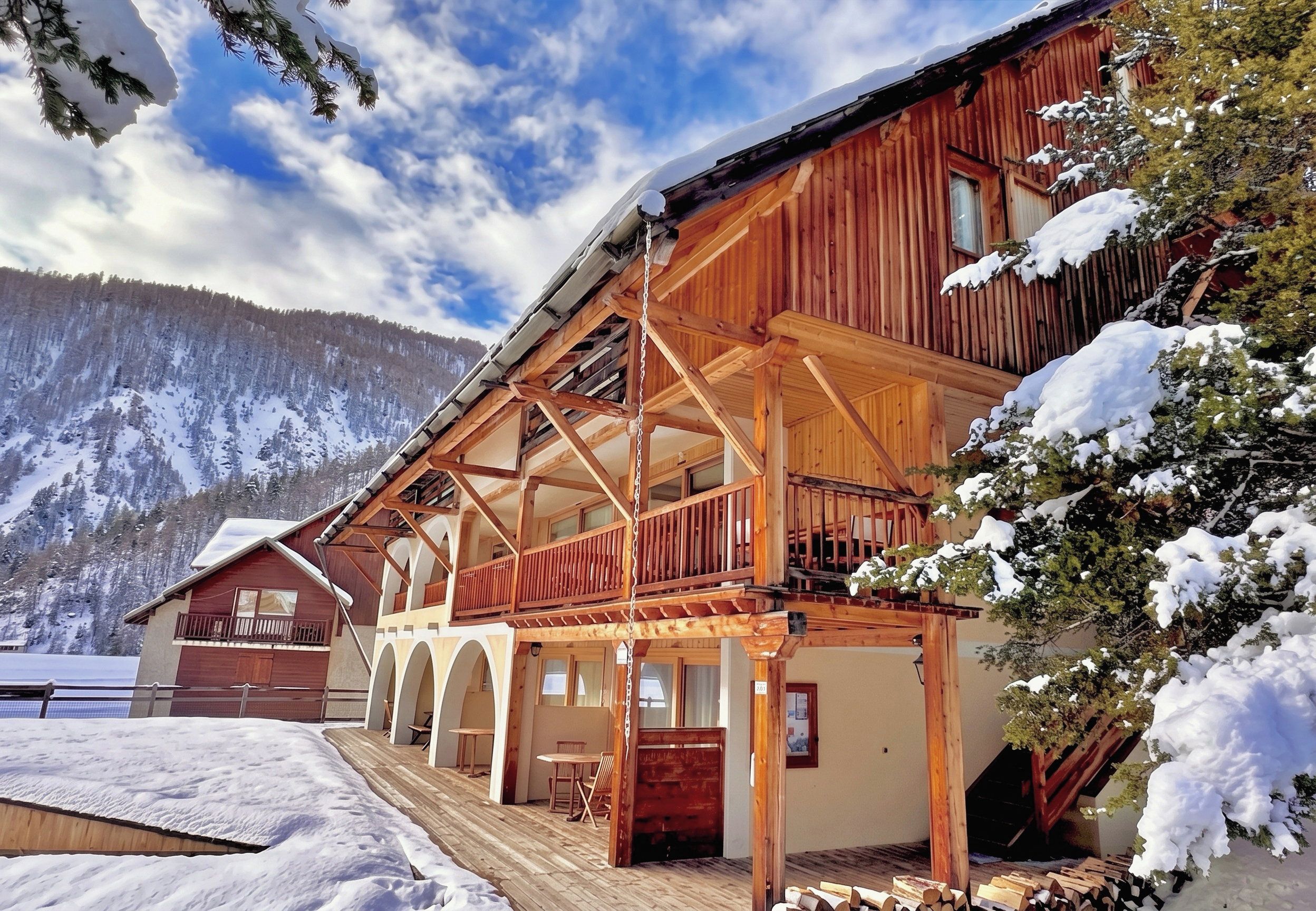Eine Holzhütte mit Balkon und überdachter Veranda, umgeben von schneebedeckten Bäumen und Bergen.