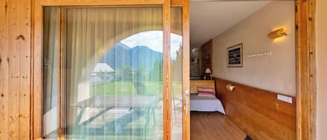 Un intérieur en bois avec une porte vitrée donnant sur un balcon, un lit avec un oreiller, une lampe fixée au mur et un tableau encadré.